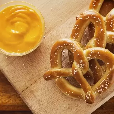 Three large, soft pretzels on a cutting board with a small container of mustard next to them. 