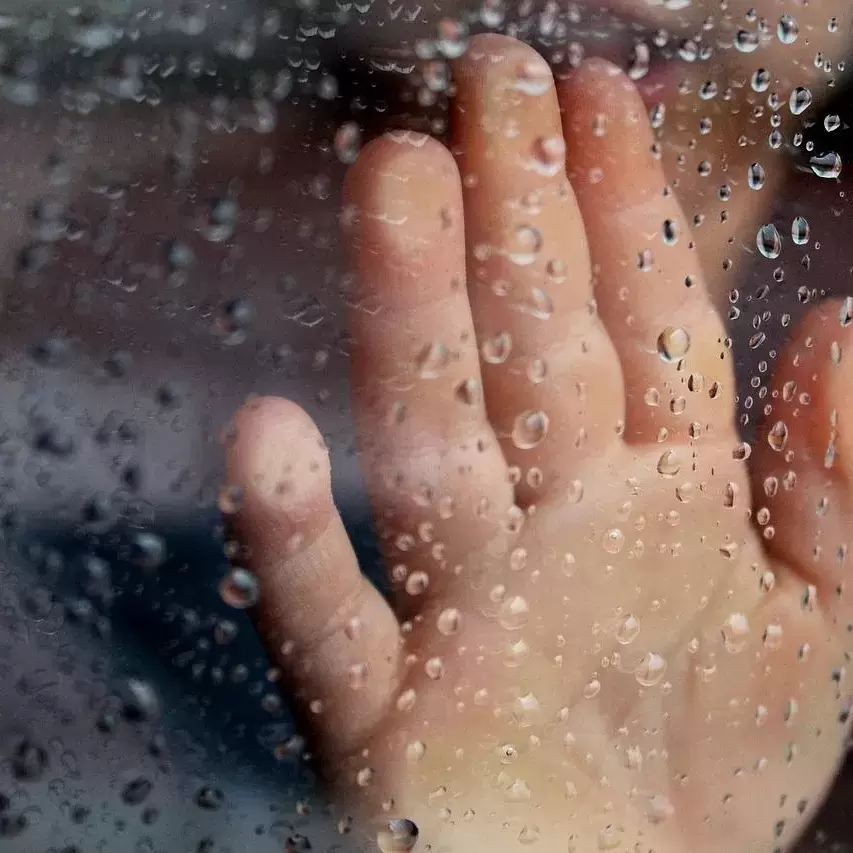 A child's hand on a window wet from rain