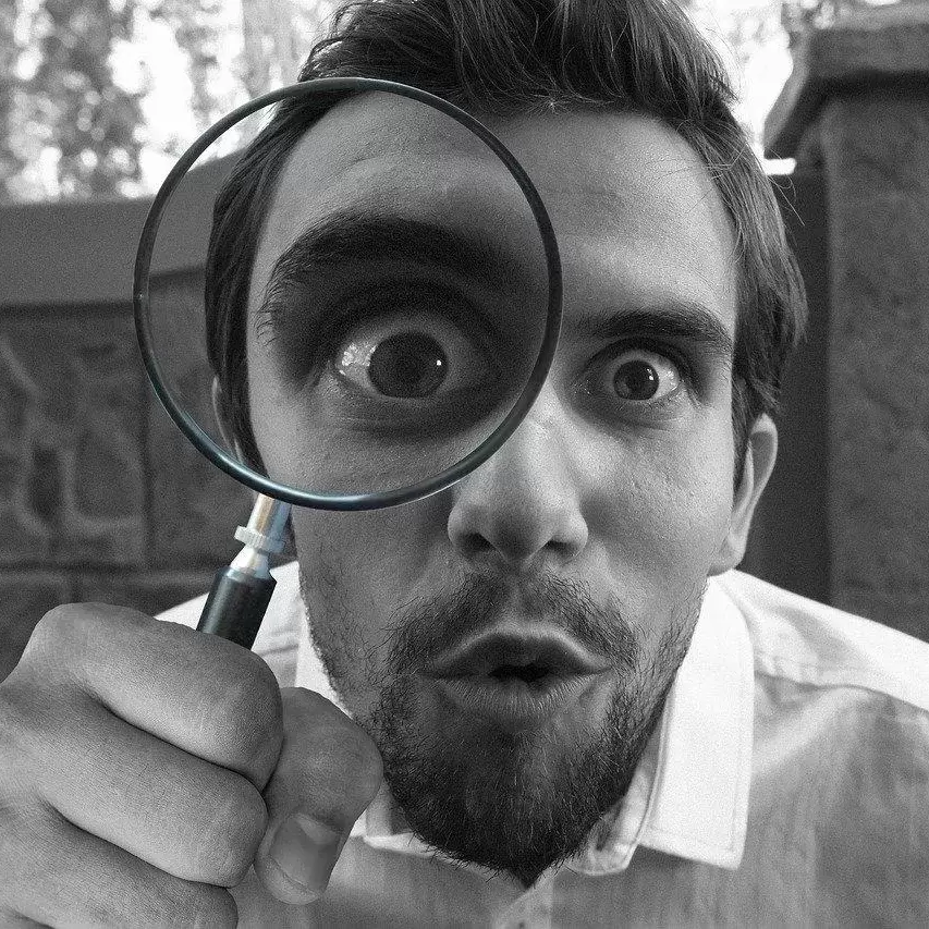 A man looking curiously through a magnifying glass